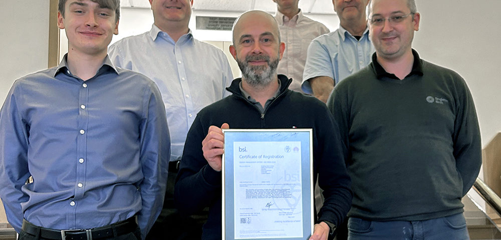 A group of people stands together and smiles for the camera. A man at center holds a framed certificate from BSI in 2023 for ISO 50001.