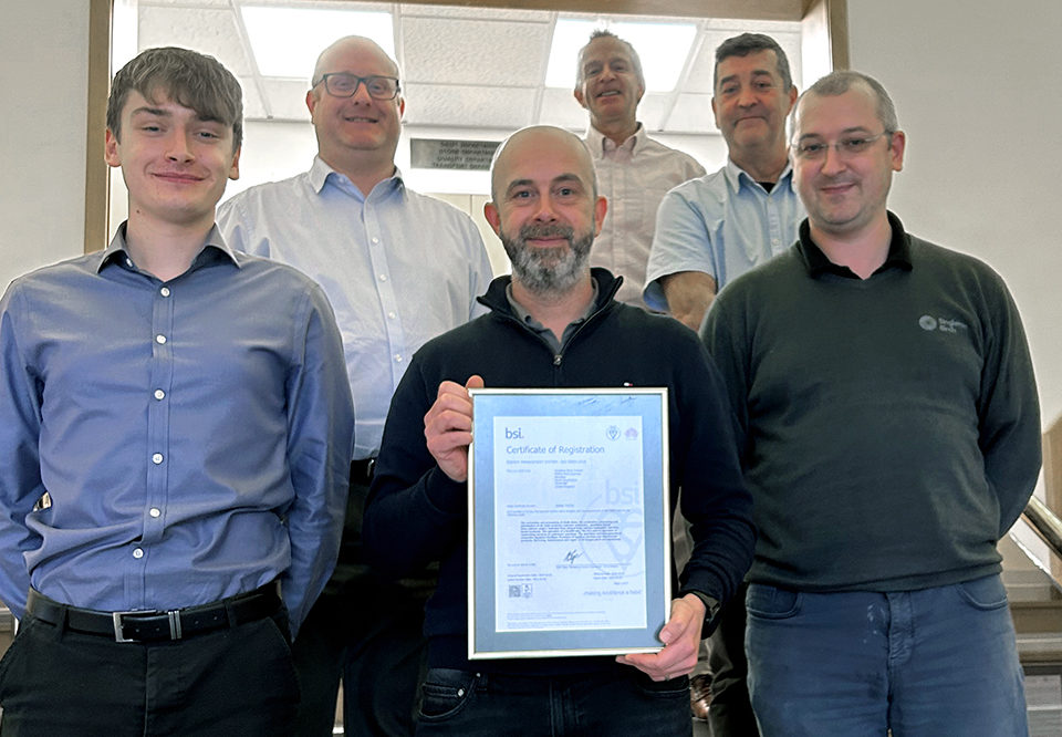 A group of people stands together and smiles for the camera. A man at center holds a framed certificate from BSI in 2023 for ISO 50001.