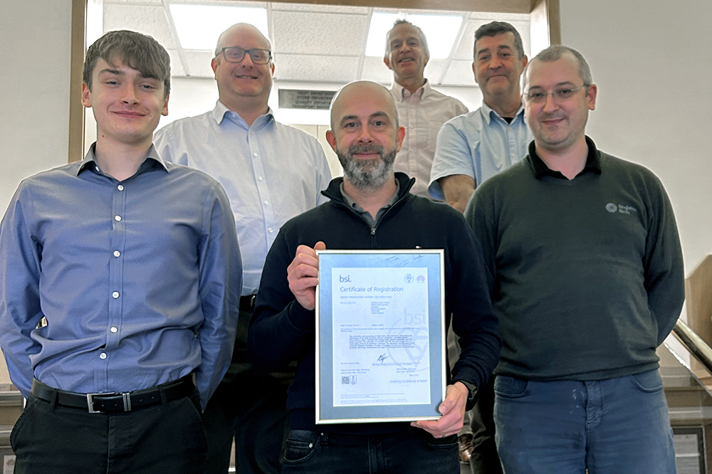 A group of people stands together and smiles for the camera. A man at center holds a framed certificate from BSI in 2023 for ISO 50001.